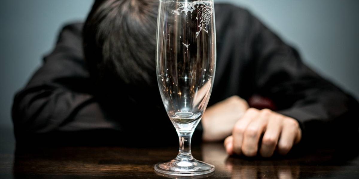 man lying facedown on table, with empty bottle in front of him