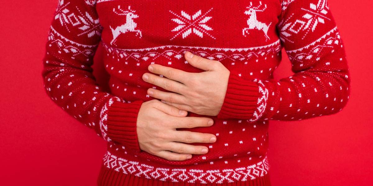 man in christmas sweater against red background gripping abdomen